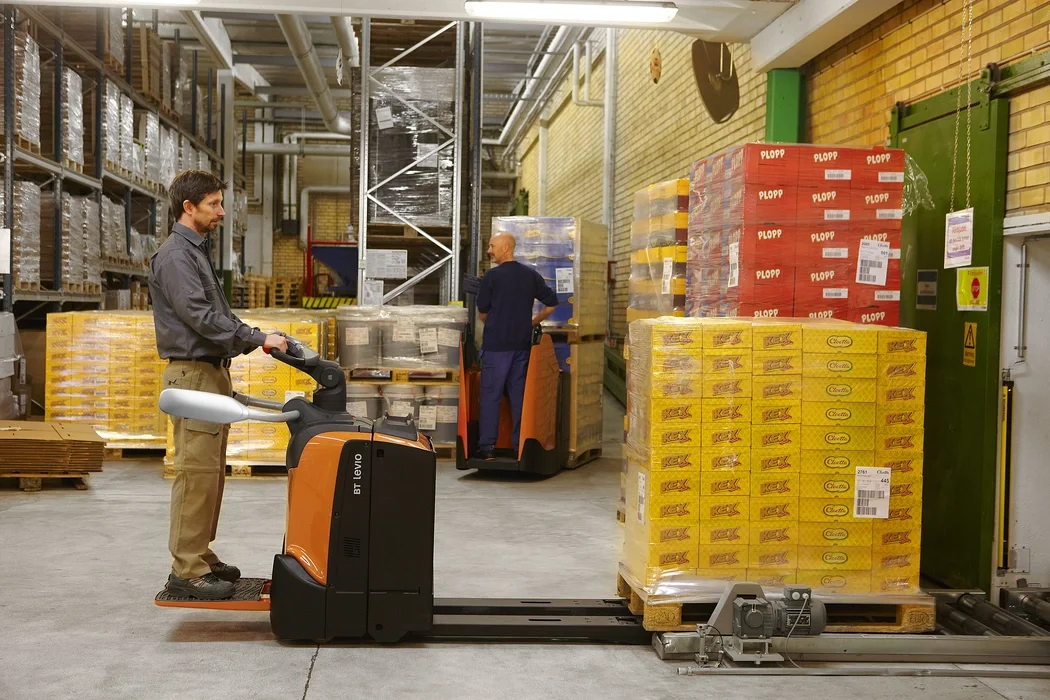 BT Levio LPE200 powered pallet truck, electric low-lifter with platform. Application photo in a warehouse environment. 