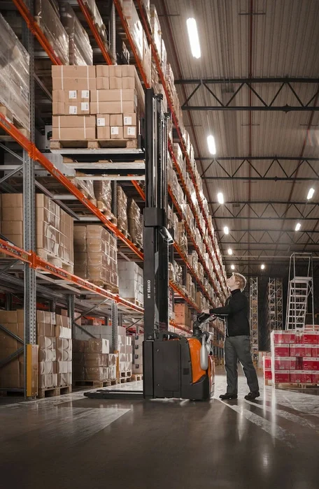 BT Staxio SPE160, electric stacker with platform and side guards. Application photo in warehouse environment.