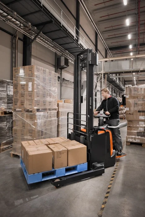 BT Staxio SPE140S powered stacker, electric stacker truck with straddle, platform, and side guards. Application photo in a warehouse environment.