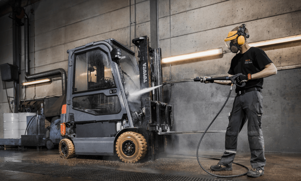 Employee washing used Toyota forklift with pressure washer