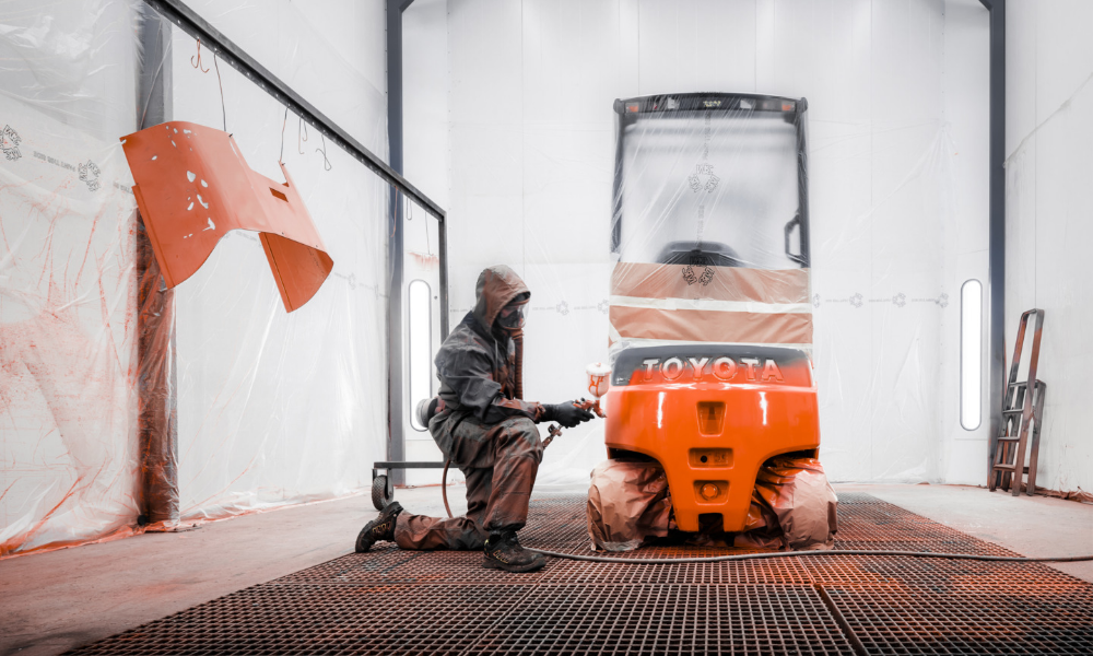 Employee spray-painting used Toyota forklift in workshop
