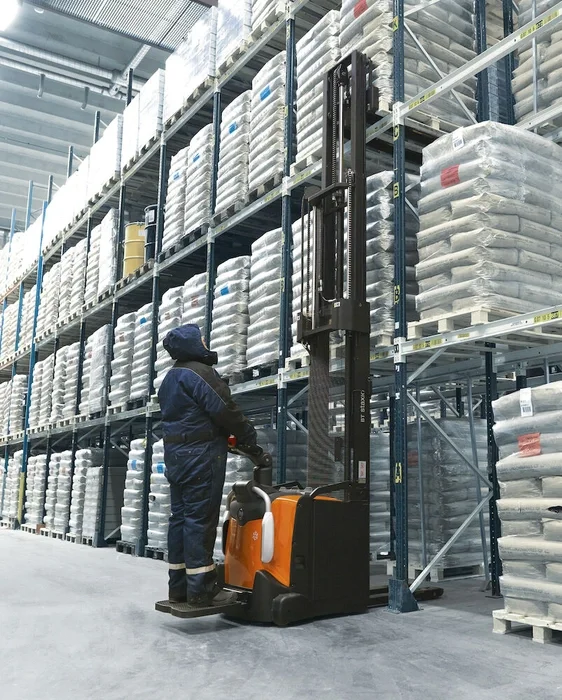 BT Staxio SPE160L, electric stacker with elevating support arms, platform, and side guards. Application photo in cold store environment.
