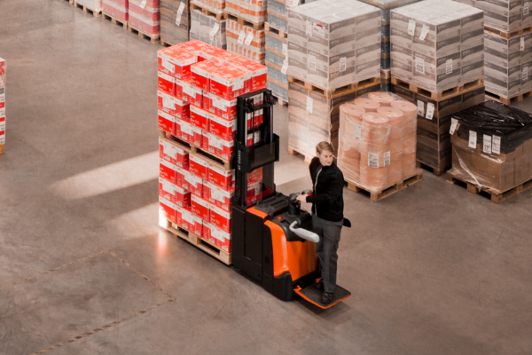 Product photo of powered stacker operated in a warehouse moving two pallets.