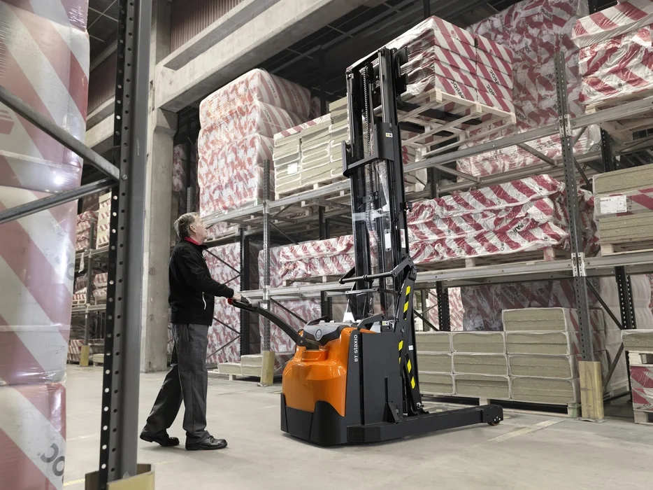 BT Staxio SWE120XR, electric walkie stacker with reach mast. Application photo in warehouse environment.