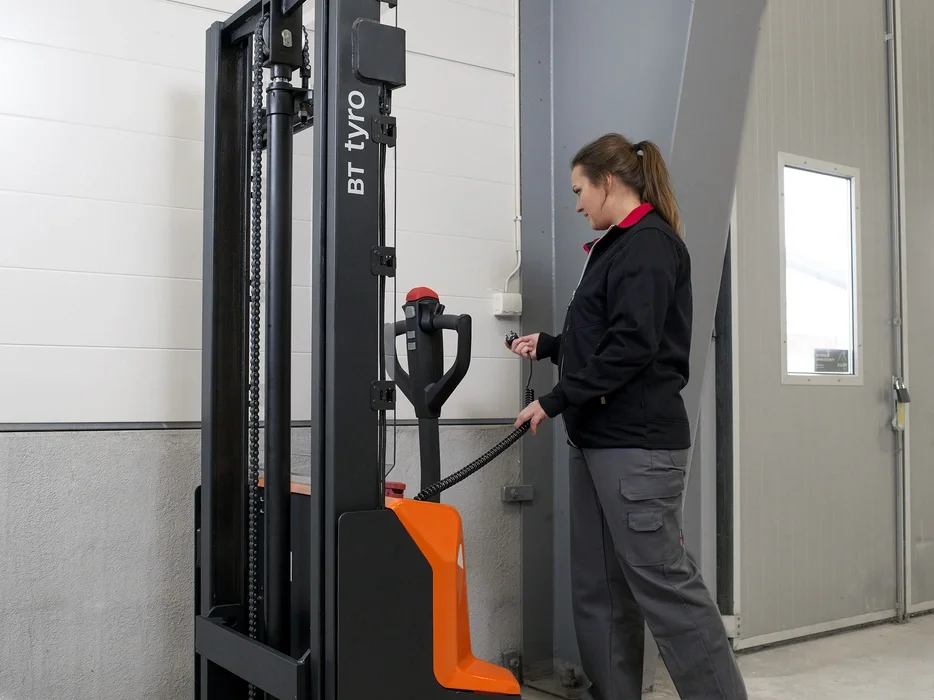 BT Tyro SHE100 walkie operated powered stacker. Application photo of charging in a warehouse environment.