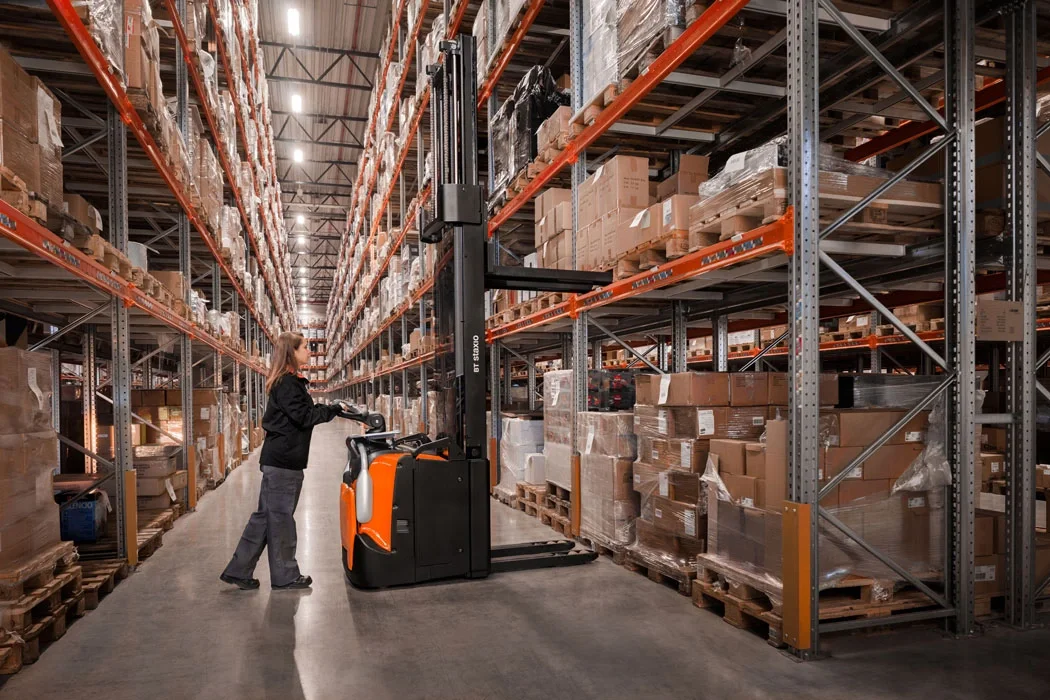 BT Staxio SPE160, electric stacker with platform and side guards. Application photo in warehouse environment.